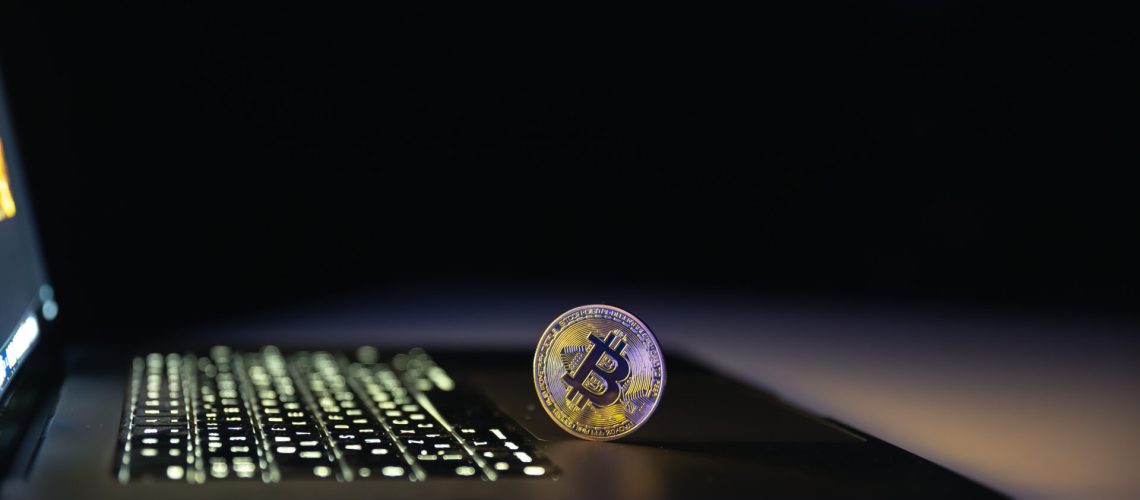 Bitcoin coin near laptop on black background. Finance and crypto money concept. High quality photo